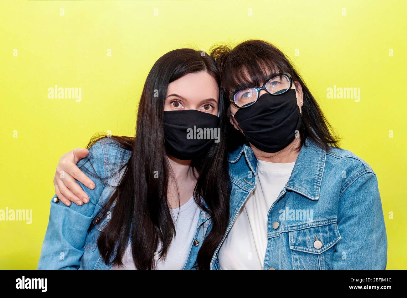 COVID-19. Madre e figlia in maschera protettiva viso medico su sfondo giallo. Concetto anti-Coronavirus. Foto Stock