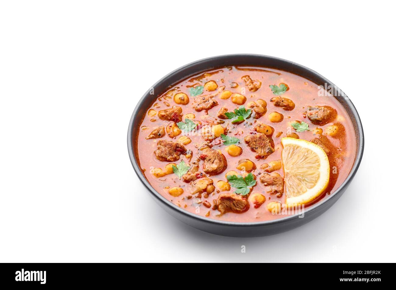 Zuppa marocchina di Harira in ciotola nera isolata su panettiera bianca. Harira è un piatto di cucina marocchina con carne di agnello o di manzo, ceci, lenticchie, pomodori Foto Stock