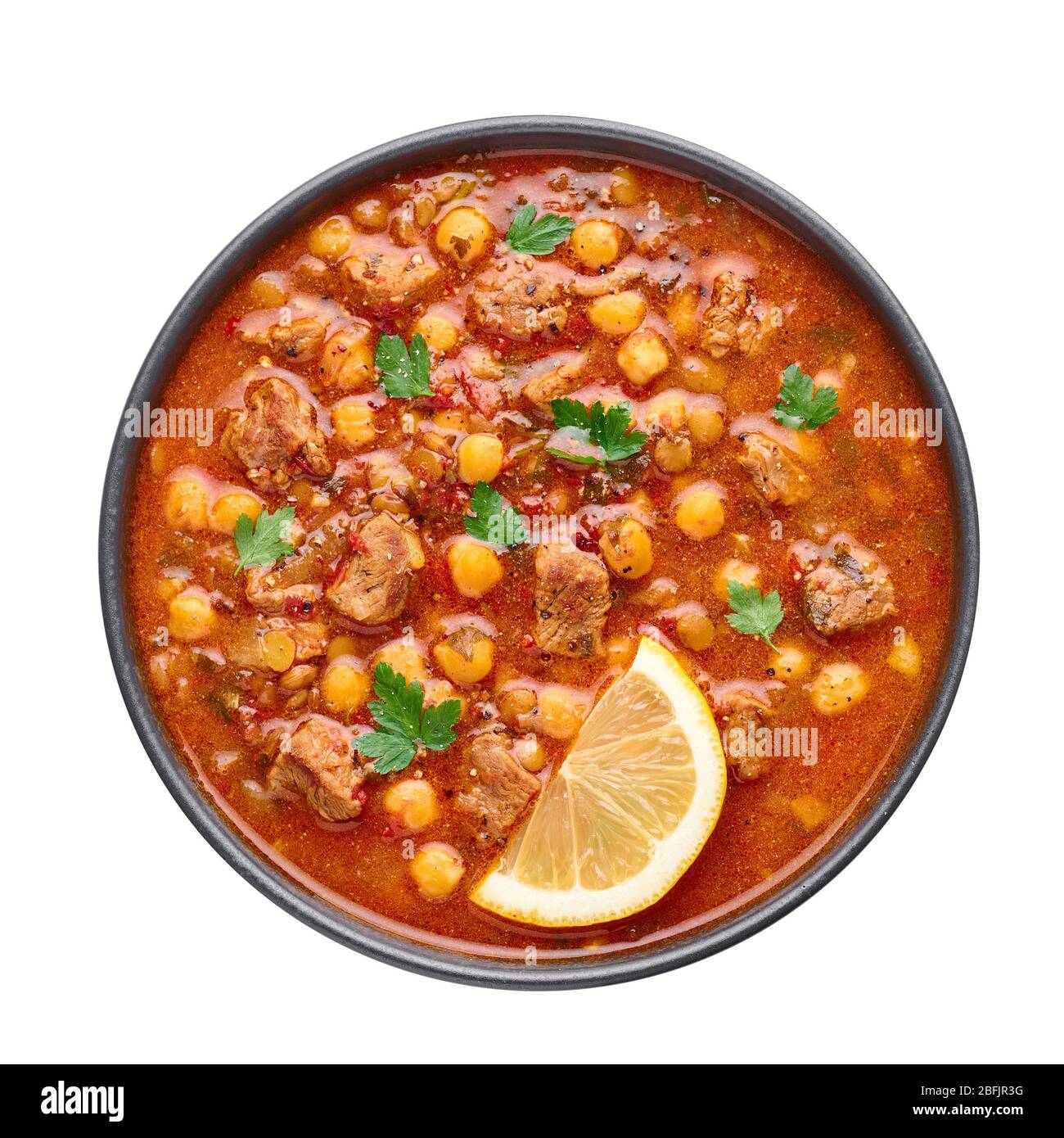 Zuppa marocchina di Harira in ciotola nera isolata su panettiera bianca. Harira è un piatto di cucina marocchina con carne di agnello o di manzo, ceci, lenticchie, pomodori Foto Stock