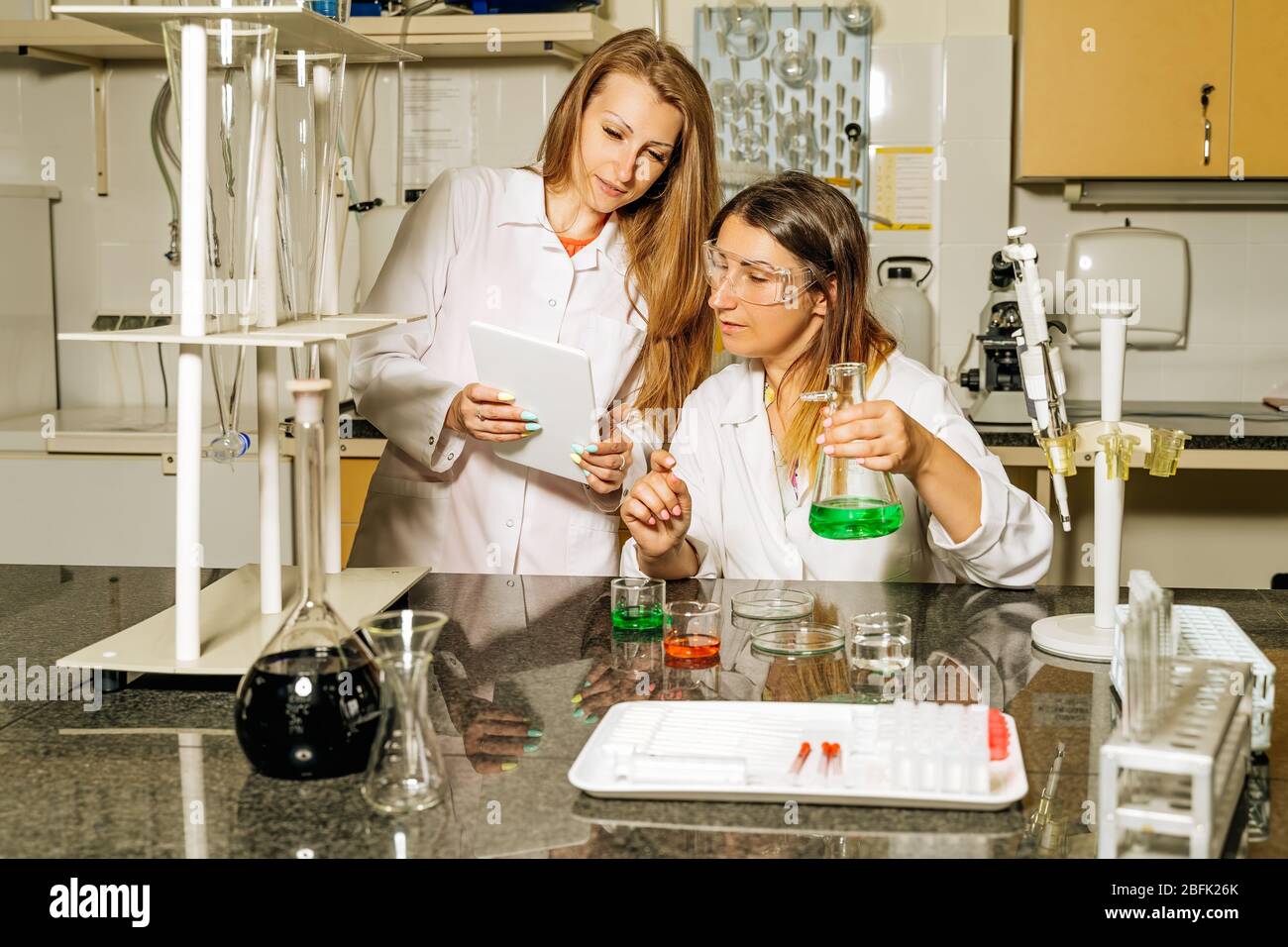 Due tecnici di laboratorio femminili che ricercano campioni medici e reagenti per la vaccinazione con coronavirus o con covid 19 e caricano i dati attraverso la compressa Foto Stock