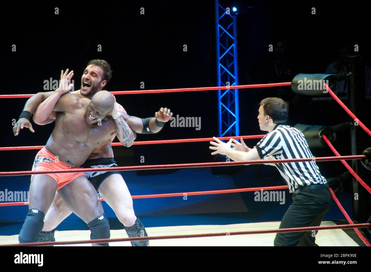 Due lottatori professionisti maschili che lottano sul ring accanto a un arbitro, in una partita di wrestling all'aperto nella città di Doha, in Qatar. Foto Stock