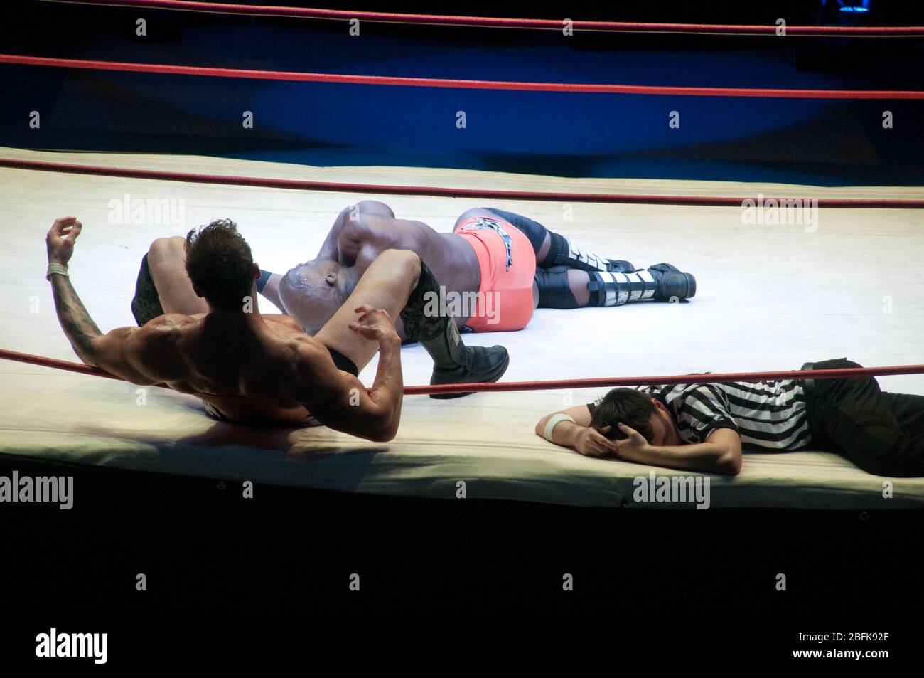 Due lottatori professionisti e un arbitro caduto e ferito sulla tela durante una partita di wrestling pro a Doha, Qatar. Foto Stock