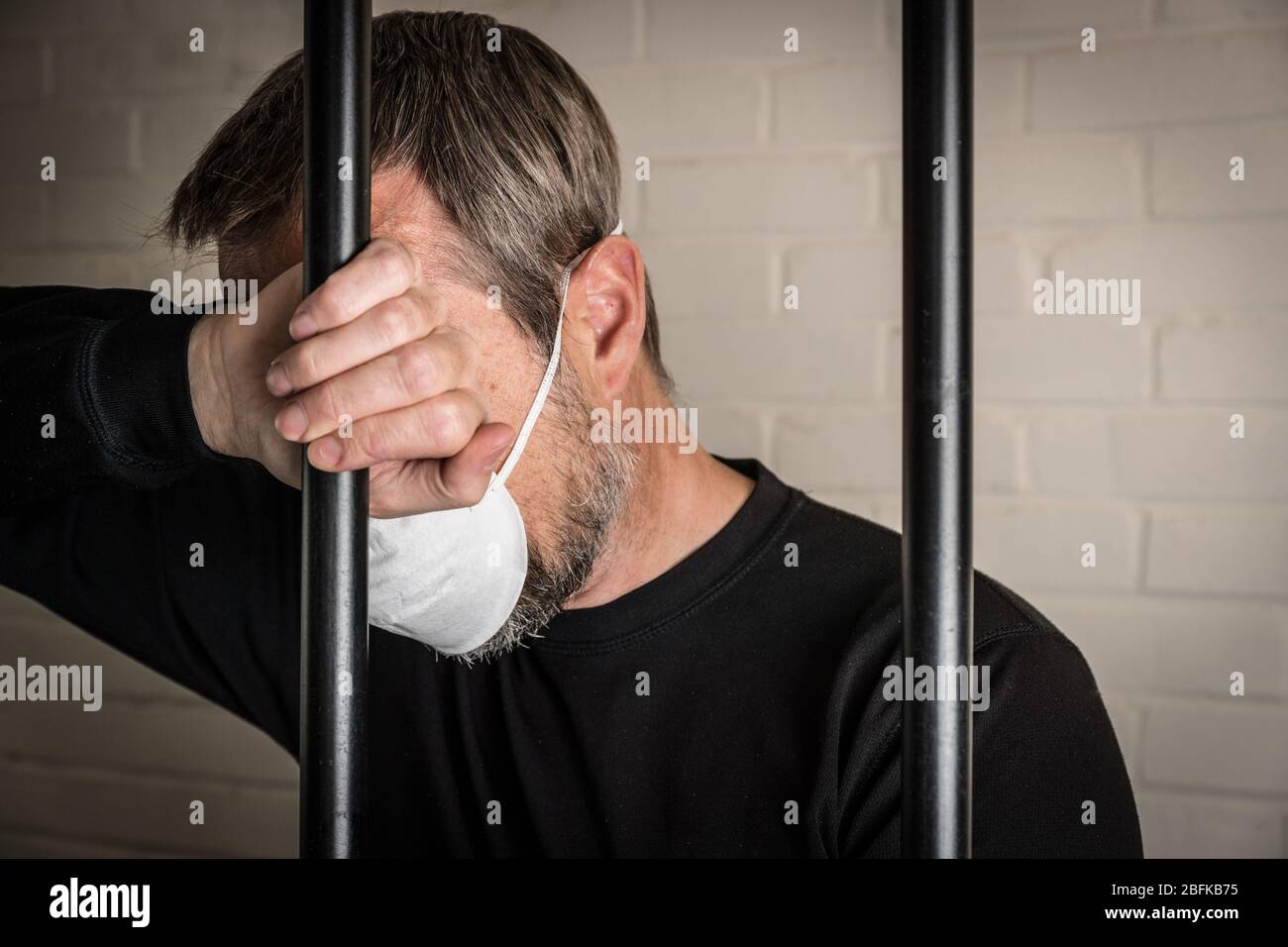 Un prigioniero dietro le sbarre che indossa una maschera facciale per illustrare Coronavirus e Covid 19 questioni in carcere. Foto posta per modello. Foto Stock