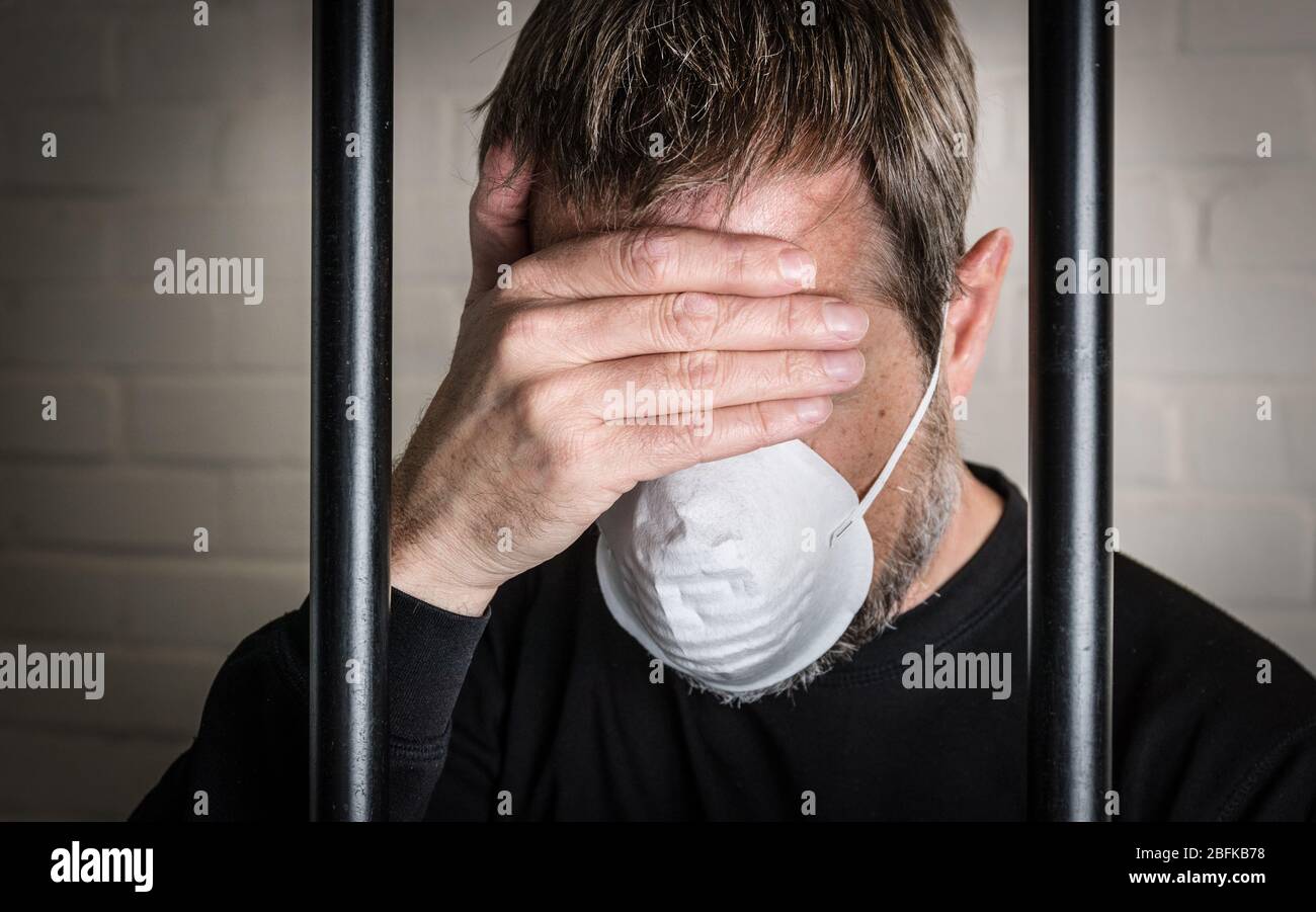 Un prigioniero dietro le sbarre che indossa una maschera facciale per illustrare Coronavirus e Covid 19 questioni in carcere. Foto posta per modello. Foto Stock