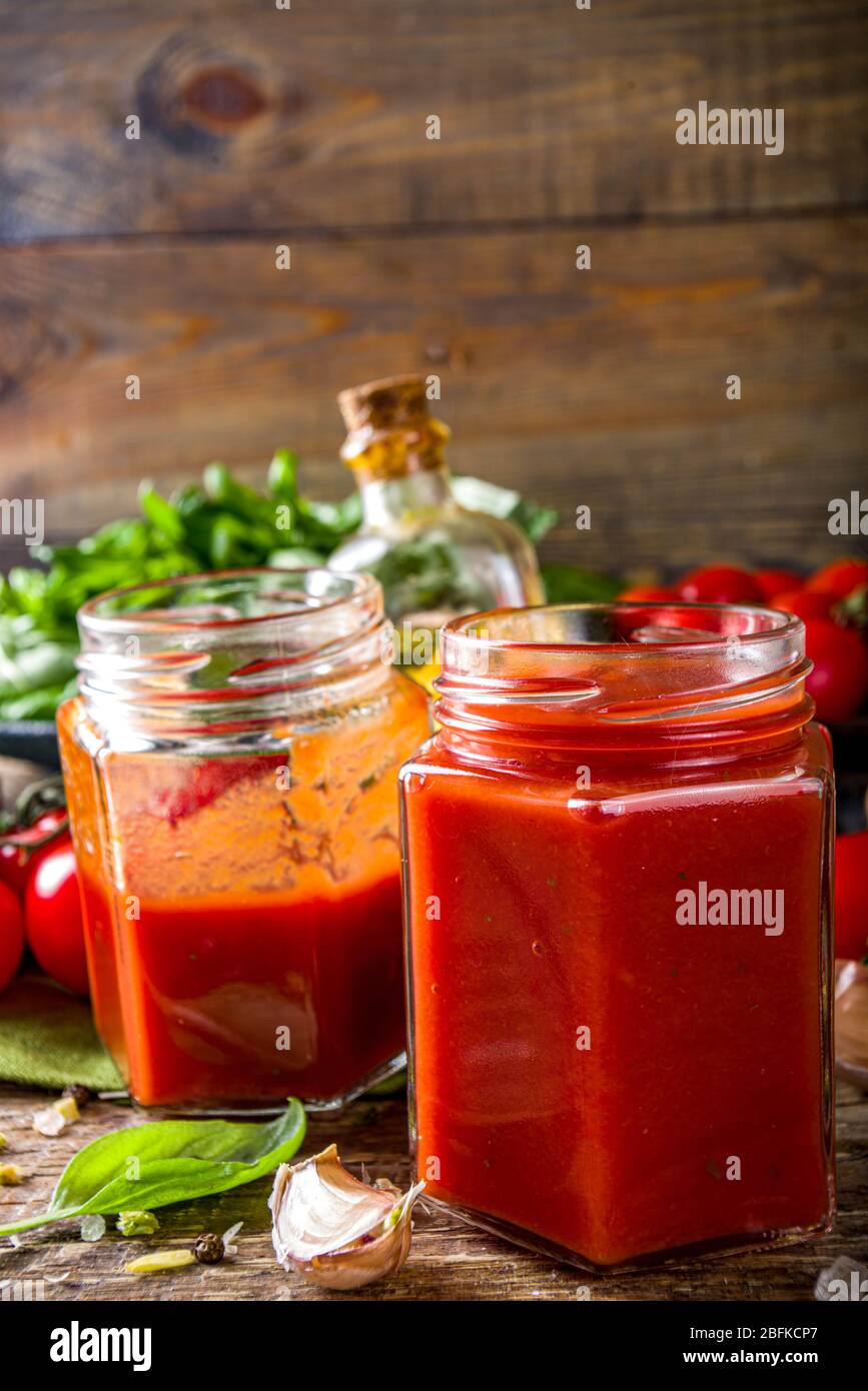 Salsa di pomodoro fatta in casa con basilico, aglio e pomodori freschi. Ketchup, salsa di marinara in piccoli vasi. Su sfondo ligneo, con verdure fresche e. Foto Stock