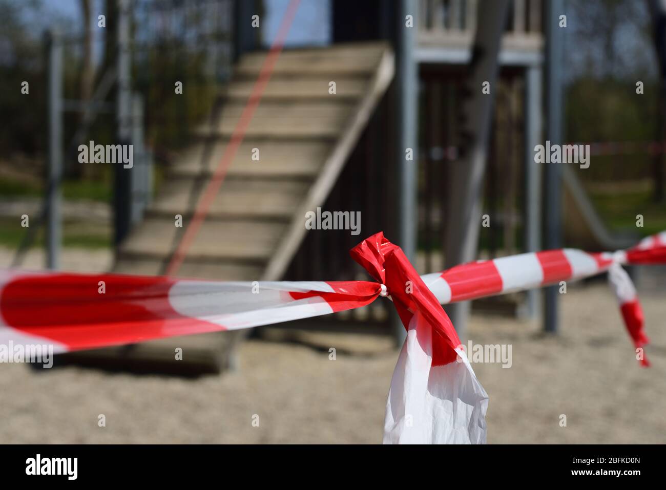 Una barriera di plastica rossa e bianca si estende davanti a un parco giochi per bambini che si trova sullo sfondo Foto Stock