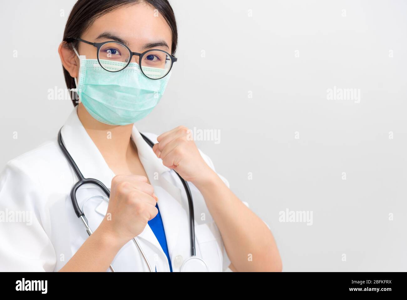 Bella giovane donna asiatica medico in uniforme bianca e maschera proteggere Coronavirus, medico sollevare i pugni per sostenere il paziente nella lotta contro le malattie Foto Stock