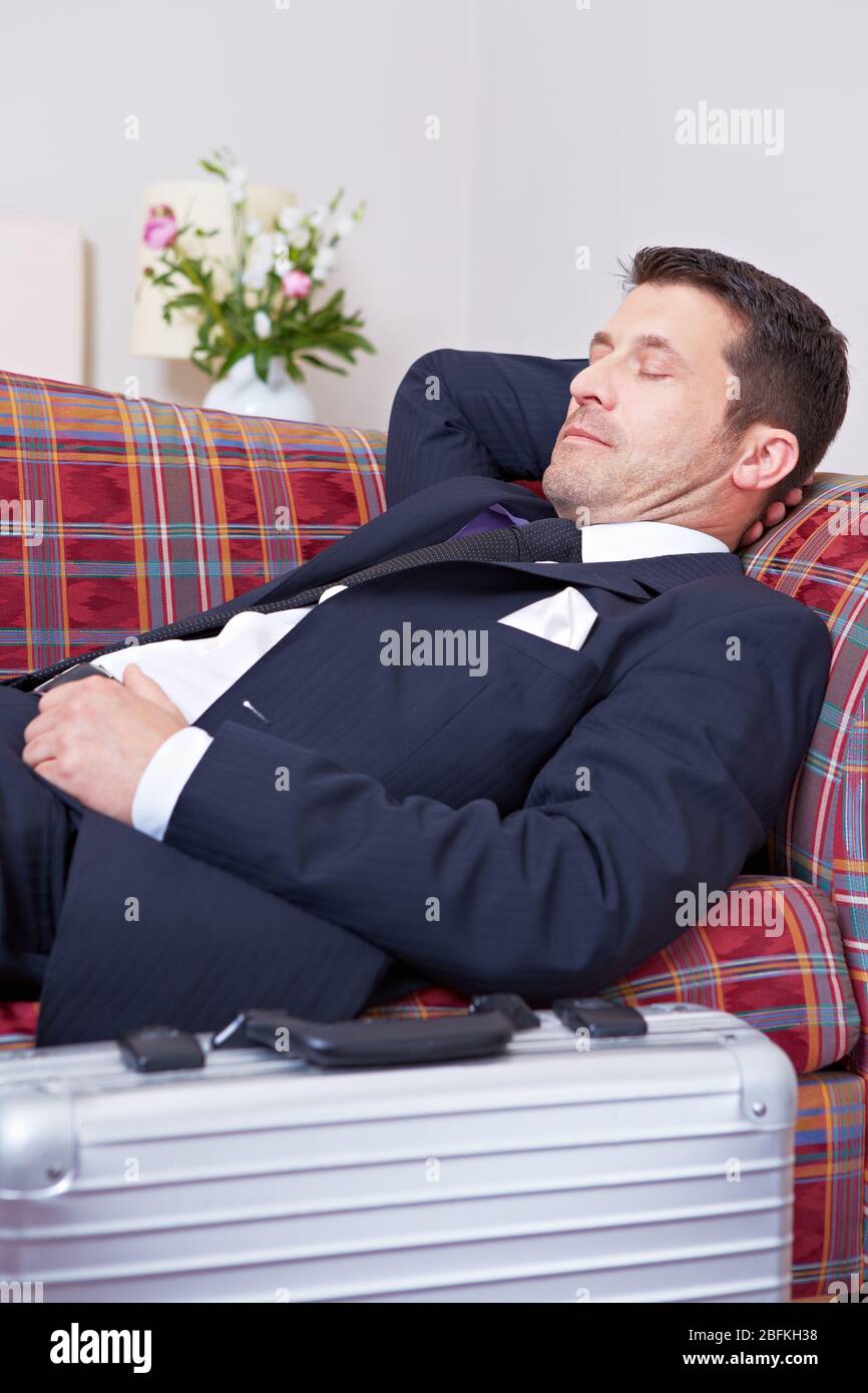 Uomo d'affari esausto dorme sul divano con valigia davanti Foto Stock