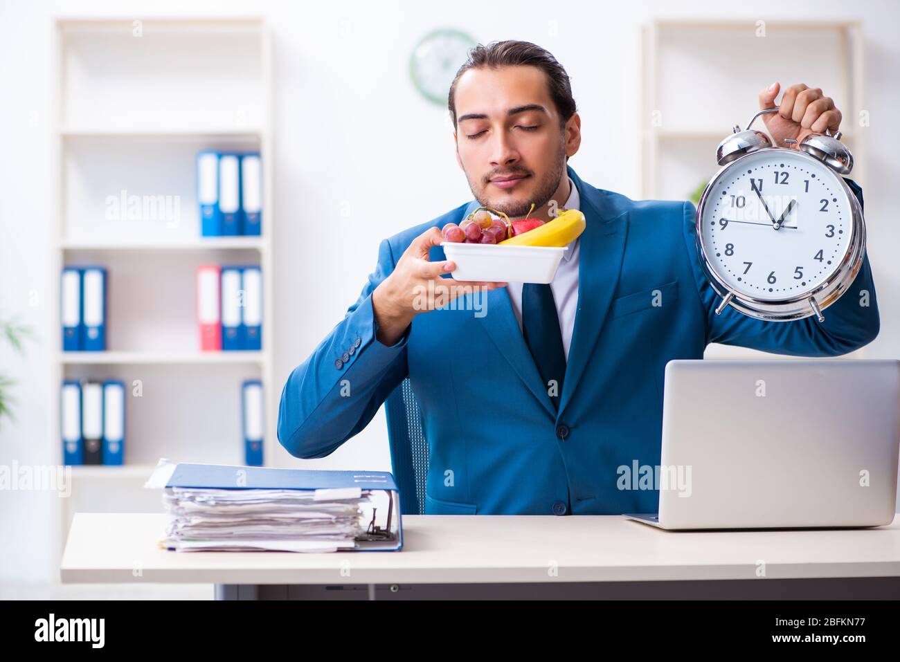 Giovane dipendente che si serve la colazione sul posto di lavoro Foto Stock