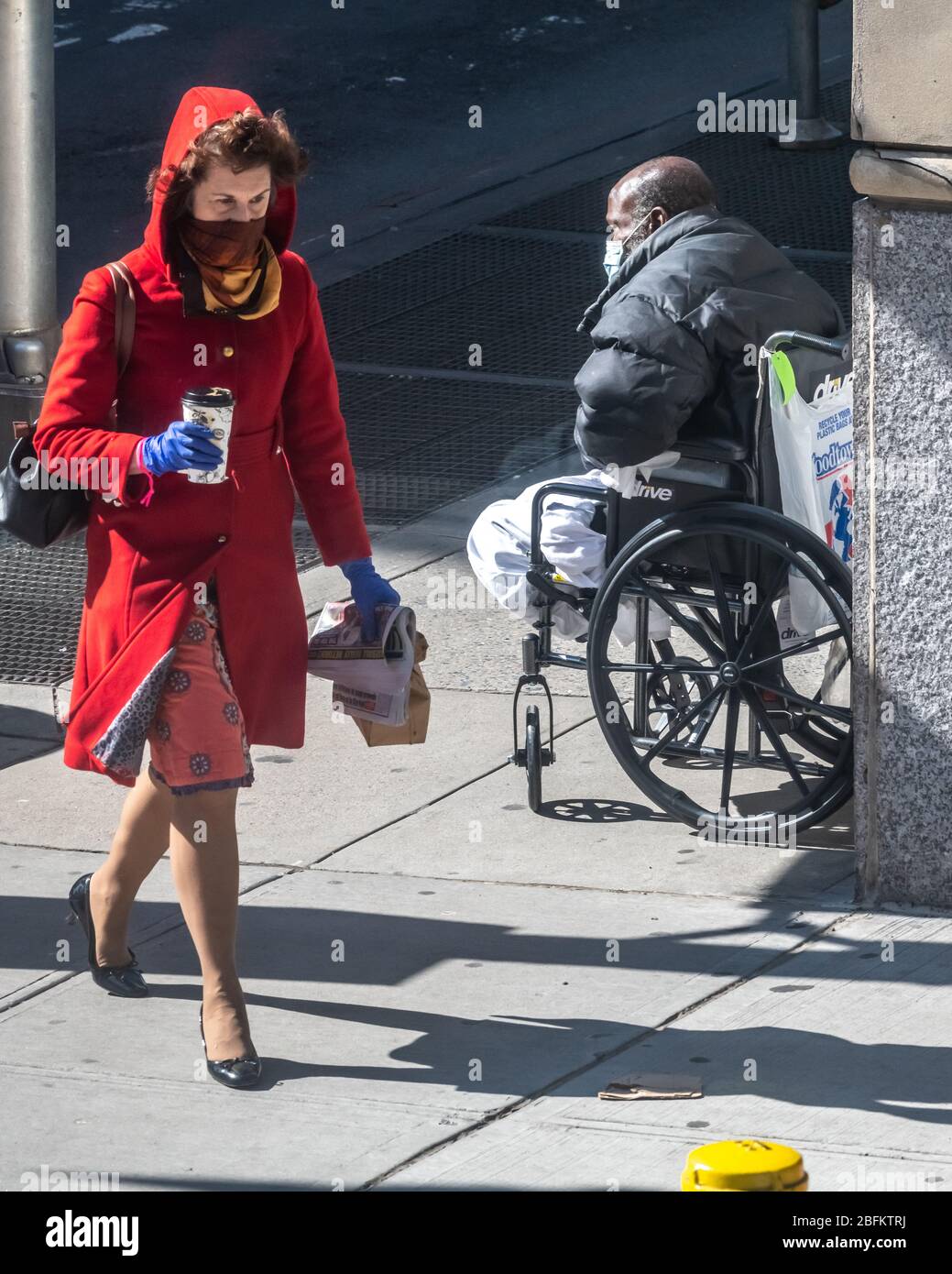 New York, Stati Uniti. 19 Apr 2020. Una donna cammina davanti a un mendicante senza tetto che indossa una maschera facciale a New York City. Il governo ha dichiarato che i newyorkers dovrebbero coprire le loro facce quando vanno fuori e non possono mantenere le distanze sociali, per evitare la diffusione del coronavirus. Credit: Enrique Shore/Alamy Live News Foto Stock