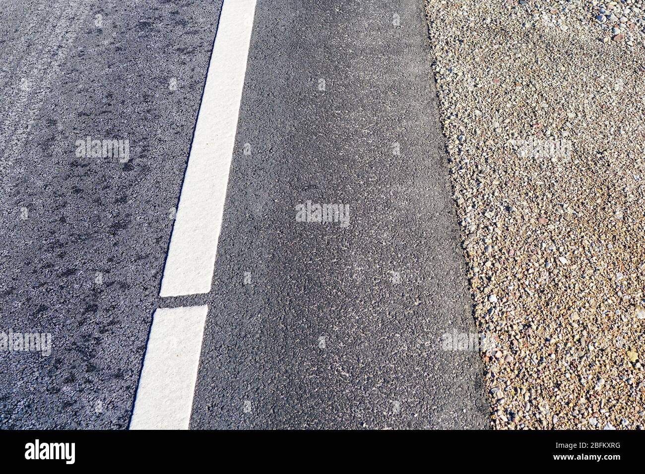 strada asfaltata con una striscia di ghiaia e una linea bianca Foto Stock