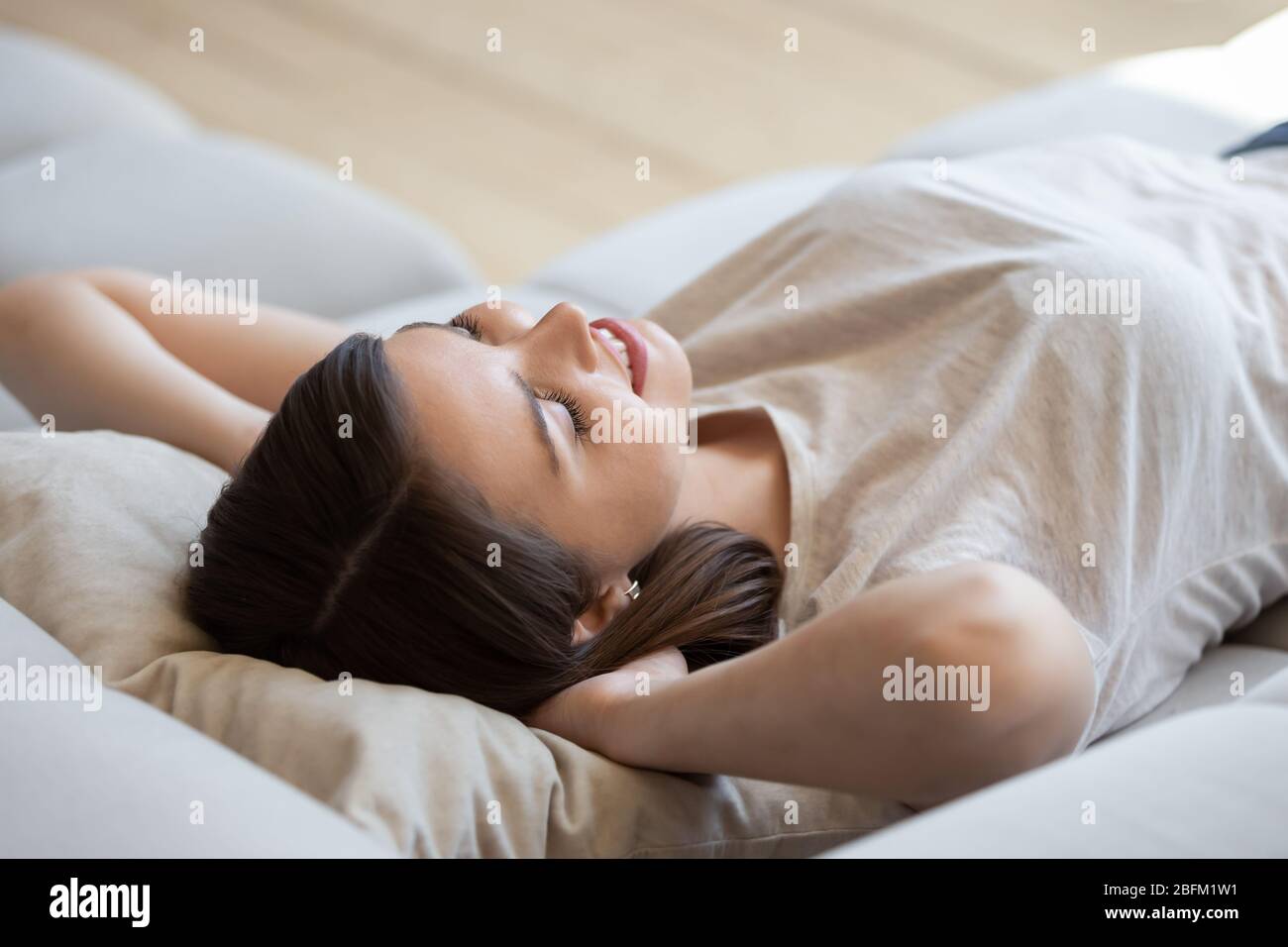 Donna felice con le mani dietro la testa sdraiata su un comodo divano. Foto Stock