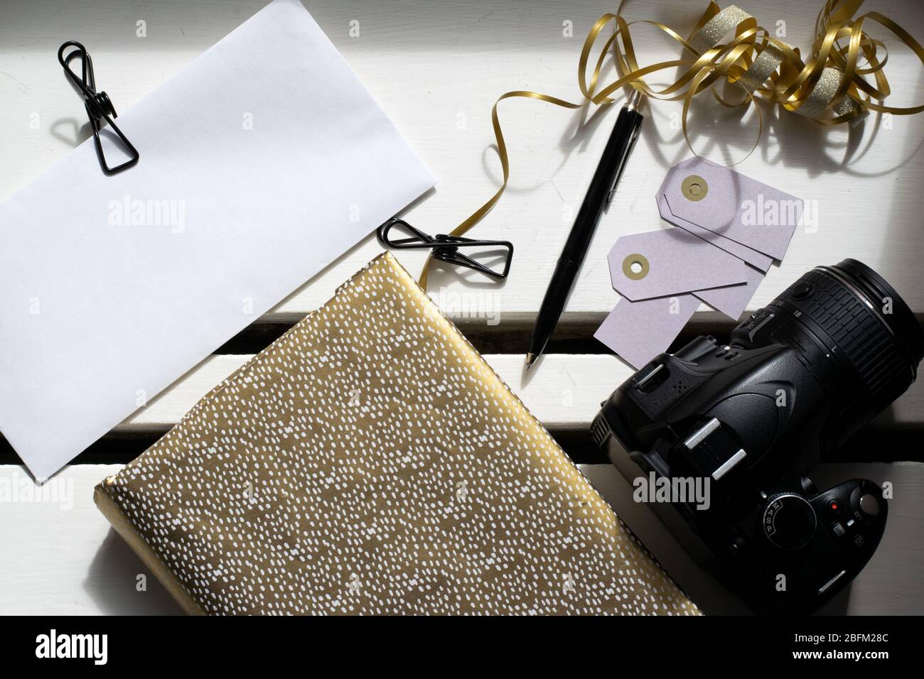 Preparazione per le feste con notebook dorato, fotocamera e clip per rilegatura su busta bianca Foto Stock