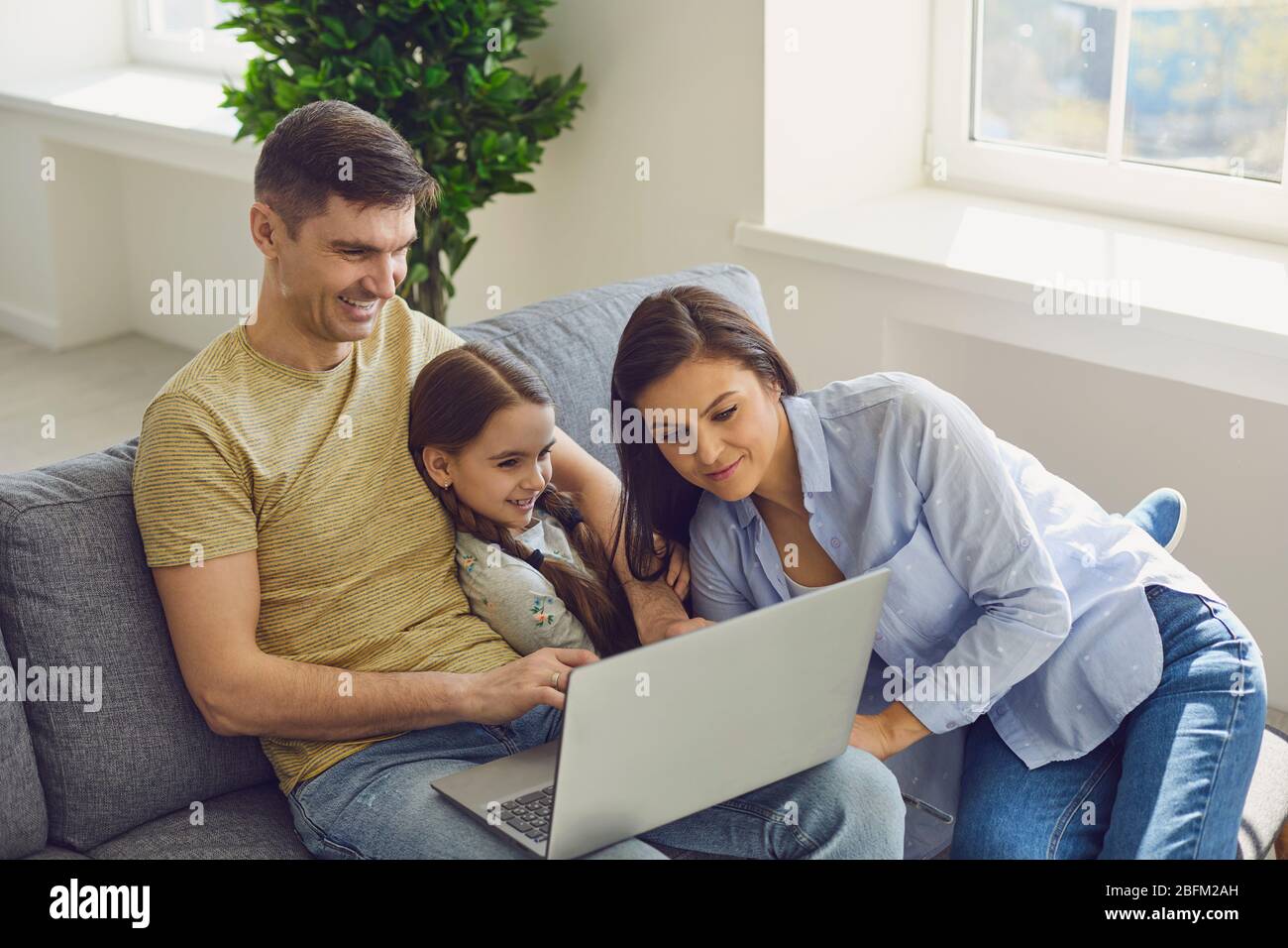 Genitori e figlia si divertono a guardare video e fare una chiamata online al notebook sorridendo a casa. Foto Stock