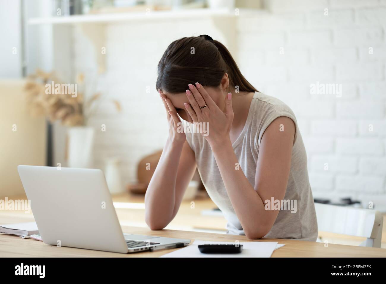 Sconvolgere la donna che tocca la testa utilizzando la calcolatrice e il laptop per il calcolo. Foto Stock