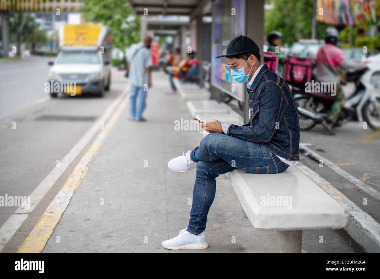 Asian Young man che usa lo smartphone in città e indossa la maschera facciale per la protezione dell'inquinamento atmosferico, delle particelle e per la protezione del virus influenzale, dell'influenza Foto Stock