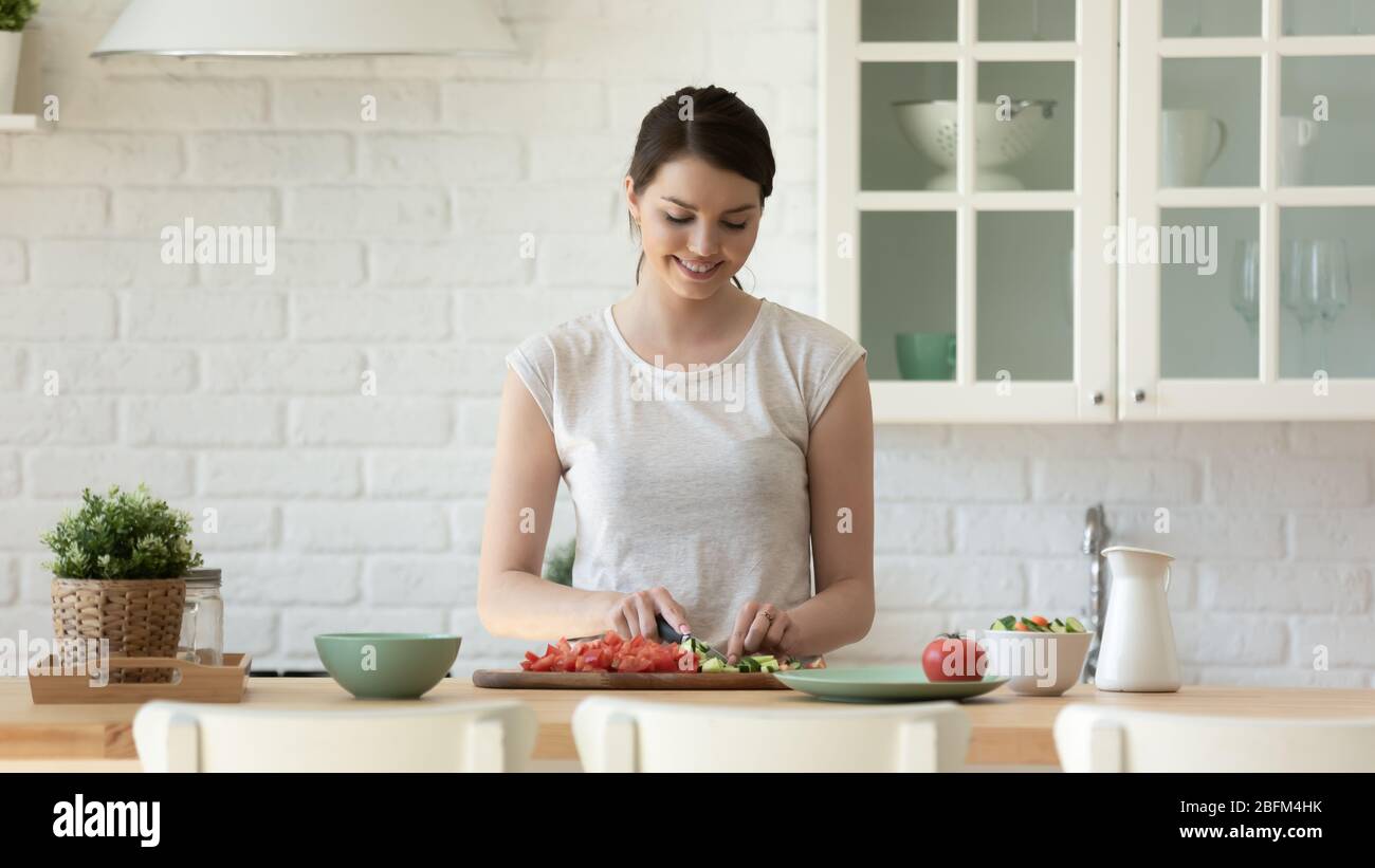 Sorridente attraente casalinga tritare verdure per cucinare insalata. Foto Stock