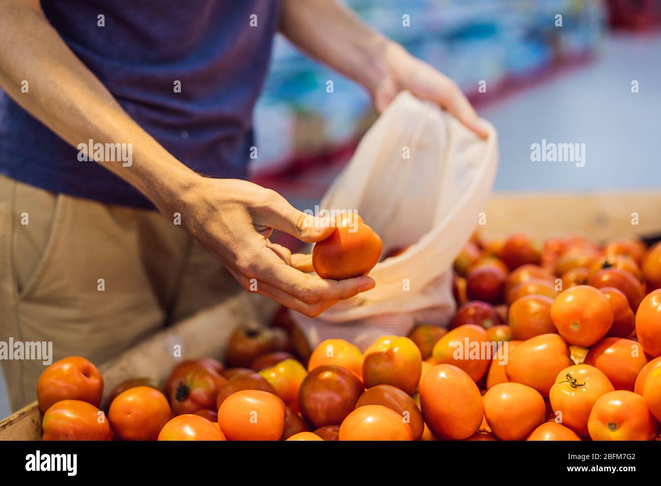 L'uomo sceglie i pomodori in un supermercato senza usare un sacchetto di plastica. Sacchetto riutilizzabile per l'acquisto di verdure. Concetto di zero sprechi Foto Stock