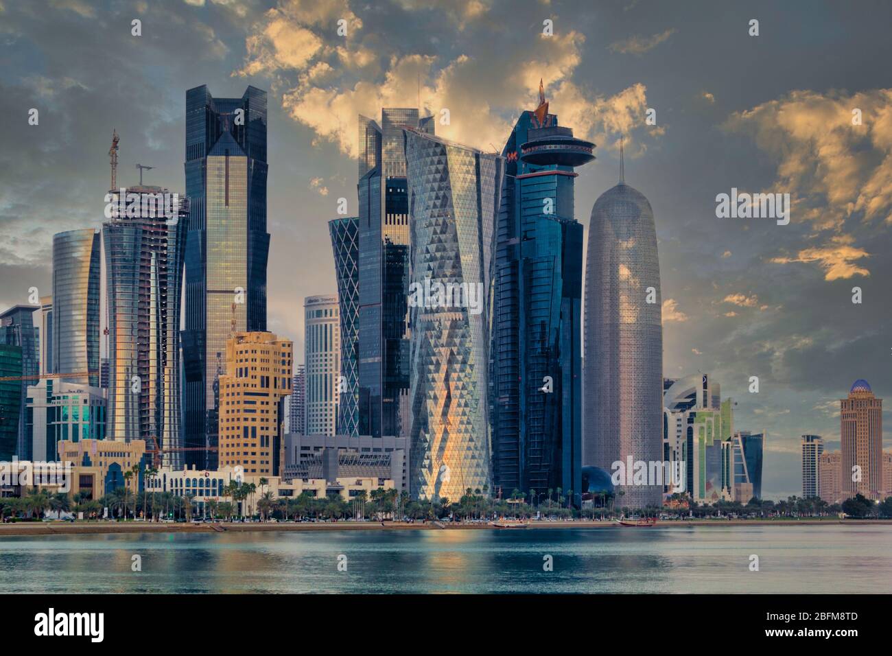 Doha Qatar skyline vista al tramonto mostra il quartiere finanziario a West Bay con moderni grattacieli, automobili, alberi e nuvole nel cielo. Foto Stock