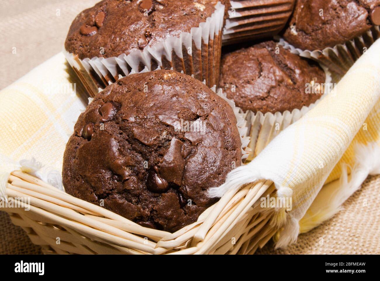 Muffin fatti in casa con scaglie di cioccolato fondente serviti in un cesto di legno rivestito con un asciugamano da cucina giallo e bianco. Foto Stock