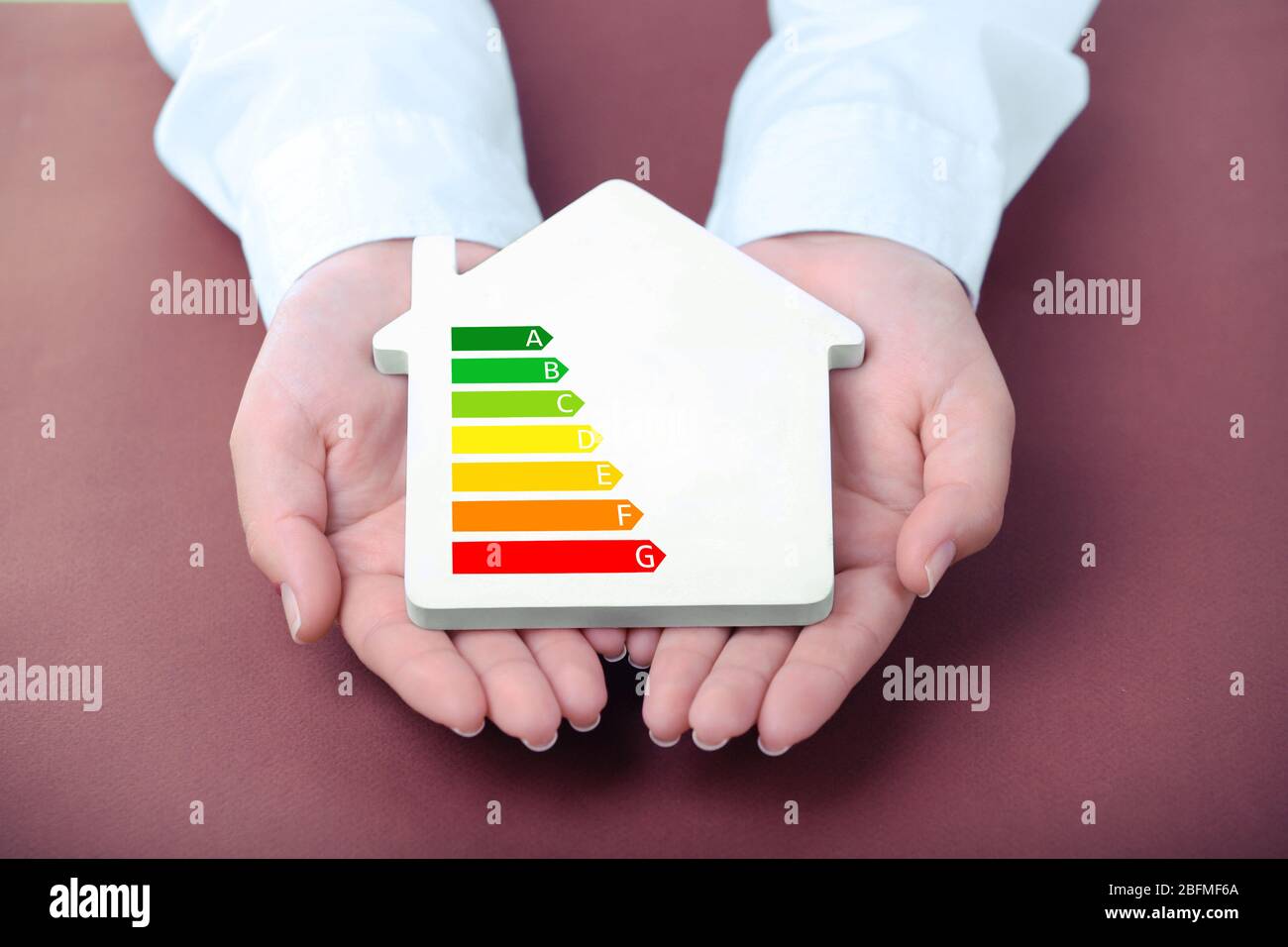Mani femminili che tengono casa con immagine in scala di efficienza energetica Foto Stock