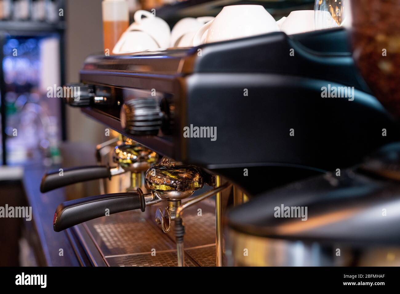 Moderna macchina da caffè con due manici in plastica nera, interruttori sopra di essi e mucchio di tazze in porcellana bianca per cappuccino Foto Stock