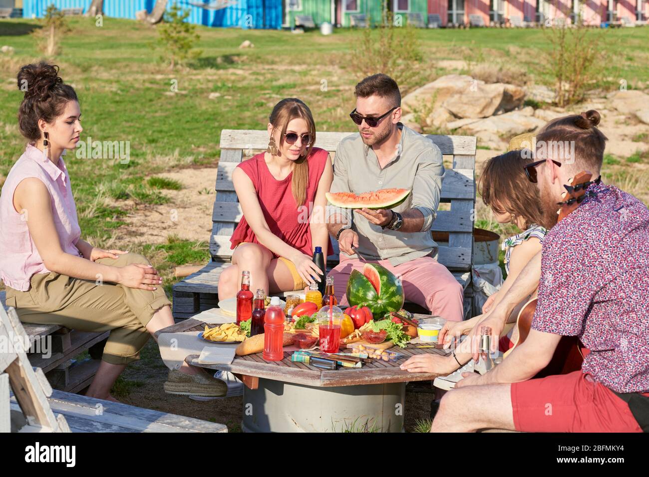 Gruppo di giovani caucasici seduti a tavola all'aperto, mangiando anguria, riposandosi e chiacchierando nella calda serata estiva Foto Stock