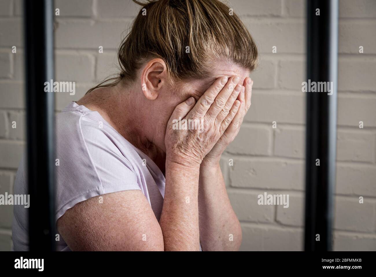Una triste prigioniera femmina sconvolsa dietro le sbarre in una prigione femminile. Immagine posta dal modello. Foto Stock