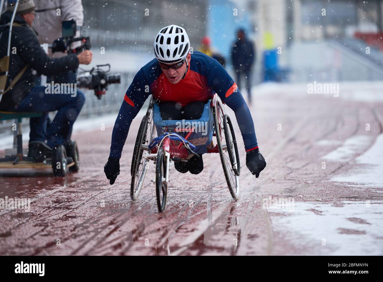 Preparazione per le paralimpiche. Determinato atleta maschile con disabilità che partecipa a gare di corse su sedia a rotelle in pista all'aperto durante la nevicata Foto Stock