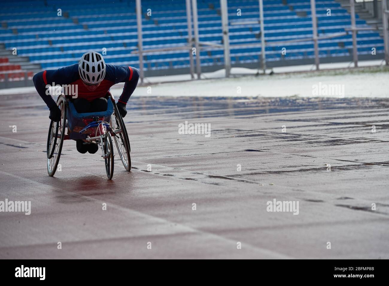 Preparazione per la maratona su sedia a rotelle. Determinato sportivo paraplegico corse in bicicletta a mano al circuito esterno e campo stadio nel pomeriggio piovoso cupo Foto Stock