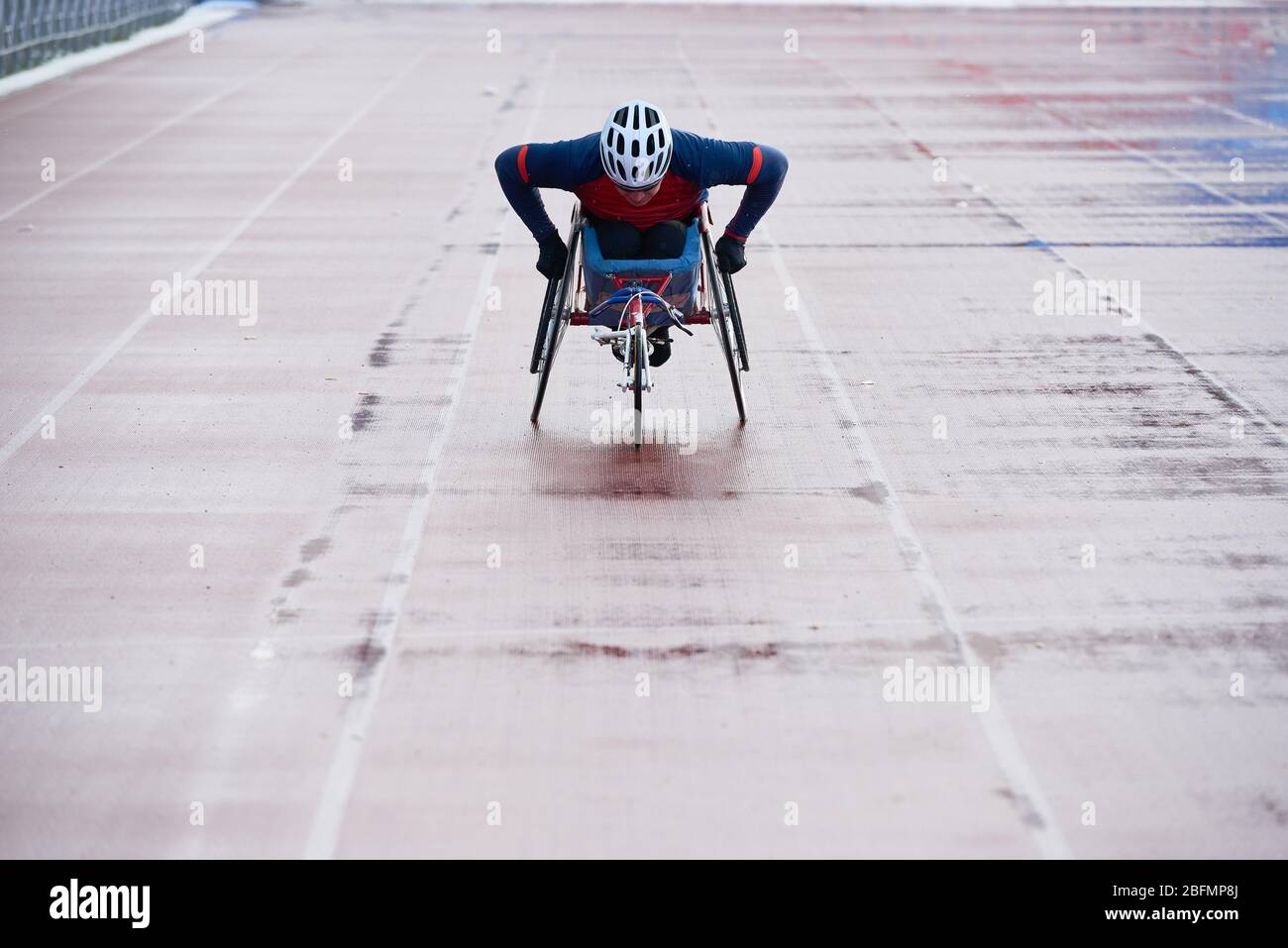 Preparazione per le paralimpiche. Determinato corridore in sedia a rotelle in abbigliamento sportivo e casco che raggiunge il traguardo durante l'allenamento al campo e pista all'aperto stadio Foto Stock