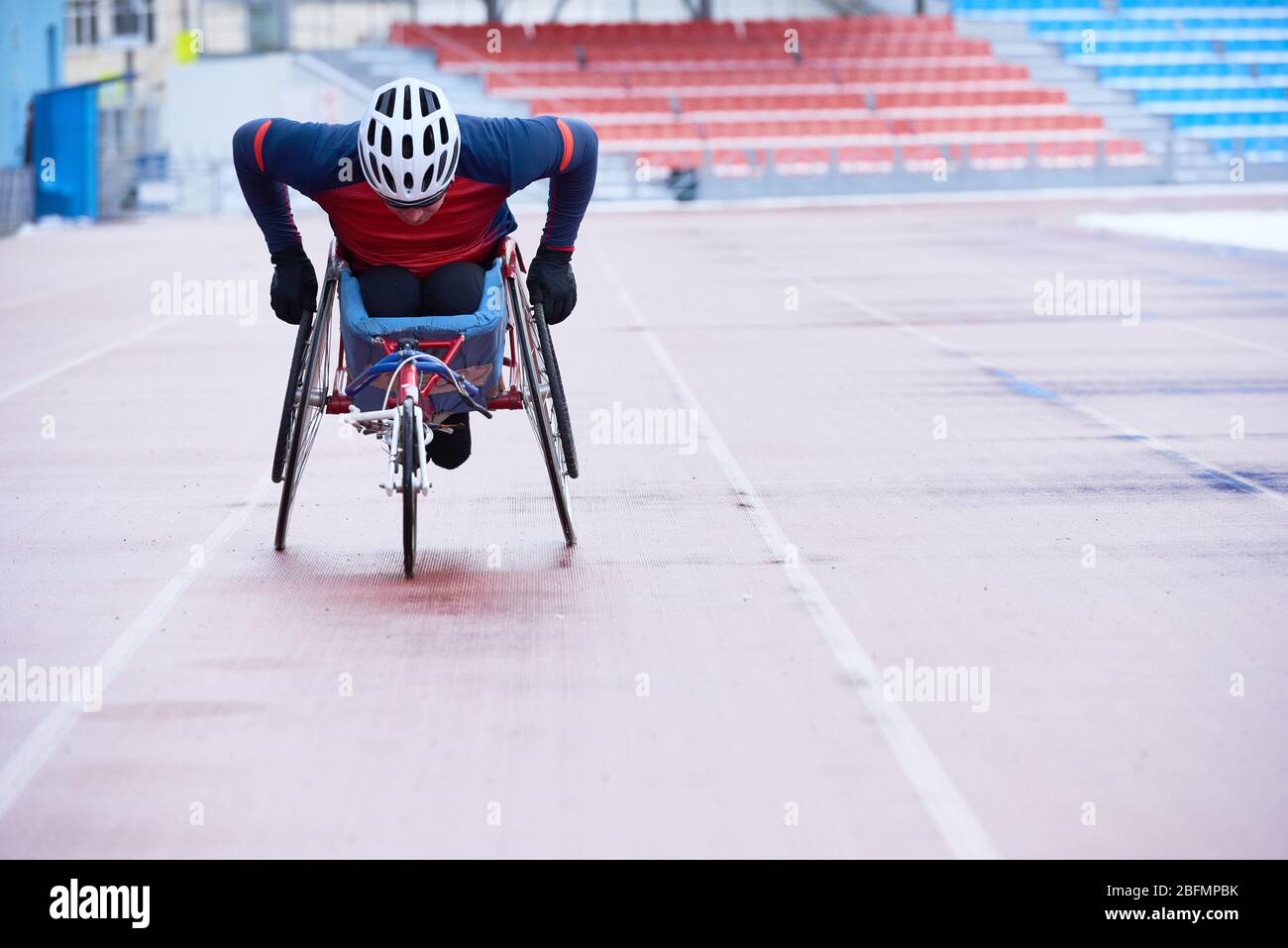 Corse su sedia a rotelle. Portatore di handicap in casco che copre la distanza in sedia a tre ruote specializzata su pista esterna Foto Stock