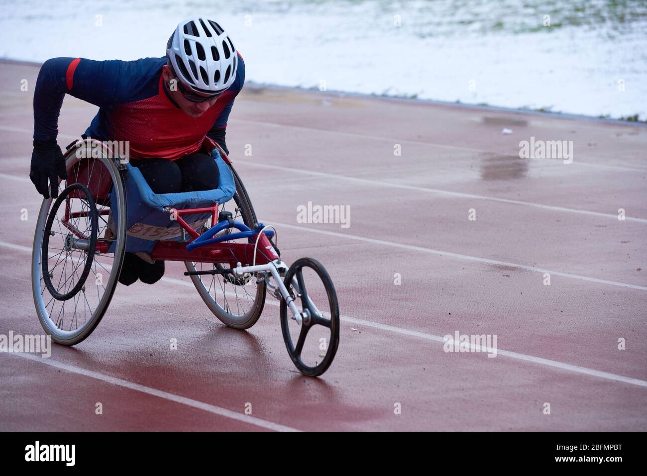 Esecuzione di prodezze sportive. Atleta maschile fortemente voluto in abbigliamento sportivo e casco in carrozzina da corsa all'aperto e stadio da campo Foto Stock