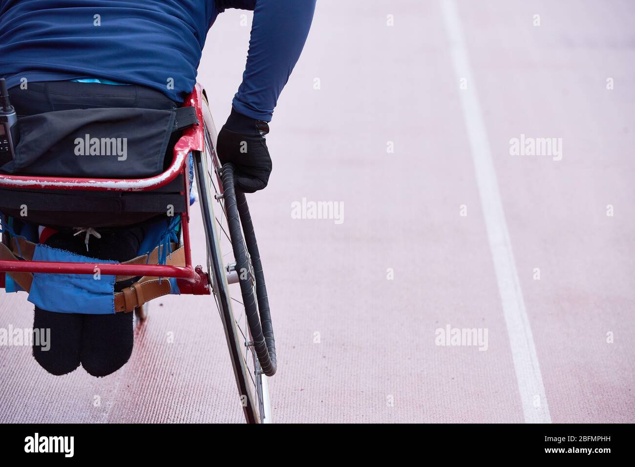 Preparazione per le paralimpiche. Vista posteriore dell'atleta fisicamente non in movimento su una sedia a rotelle da corsa in pista Foto Stock