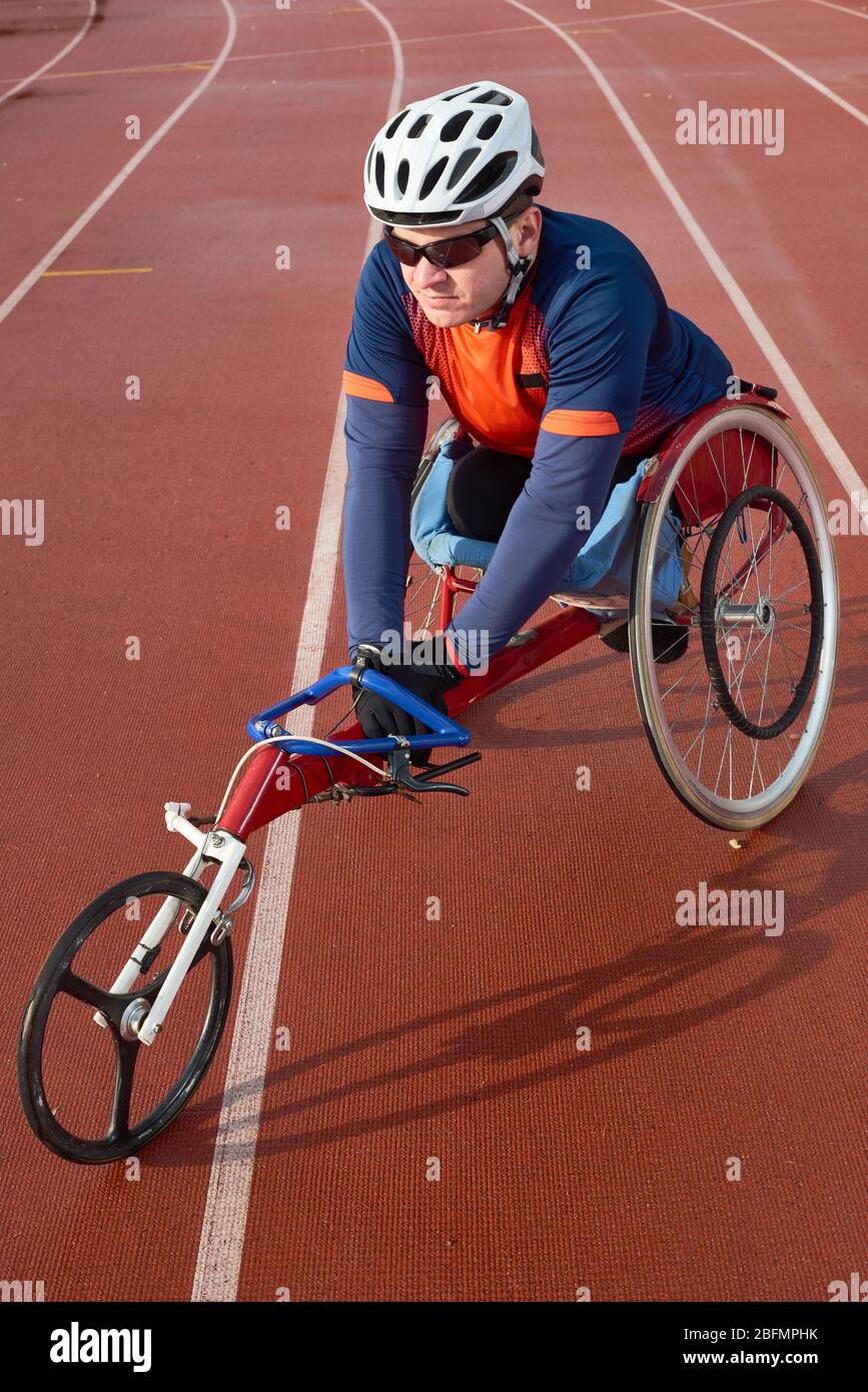 Futuro campione Paralimpico. Atleta disabile in abbigliamento sportivo e casco seduto in sedia a rotelle da corsa e concentrato prima di gareggiare in pista Foto Stock