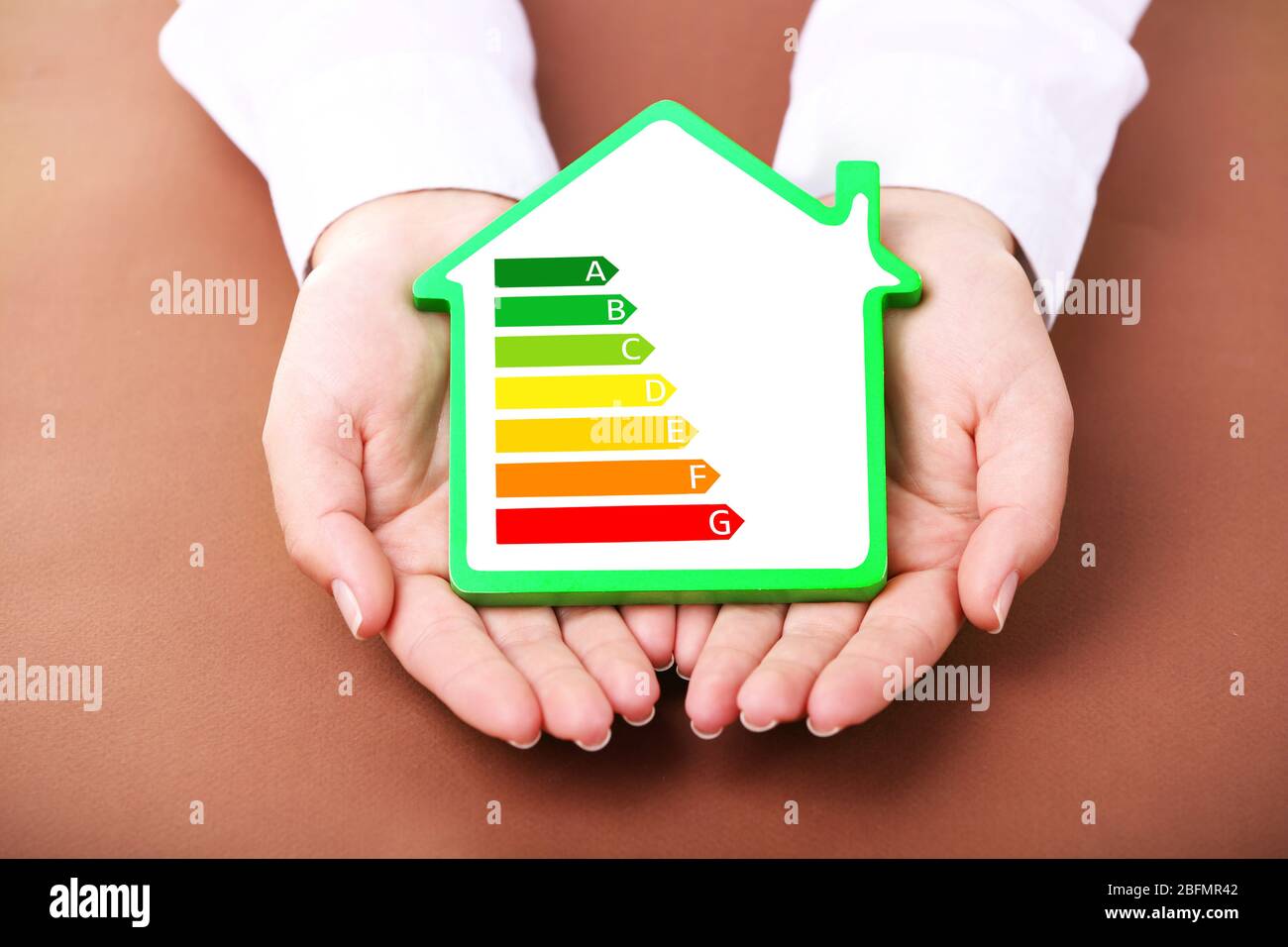 Mani femminili che tengono casa con immagine in scala di efficienza energetica Foto Stock