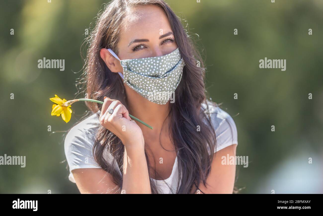 La ragazza bruna in natura indossa la maschera sorridente, tenendo un daffodil in mano. Foto Stock