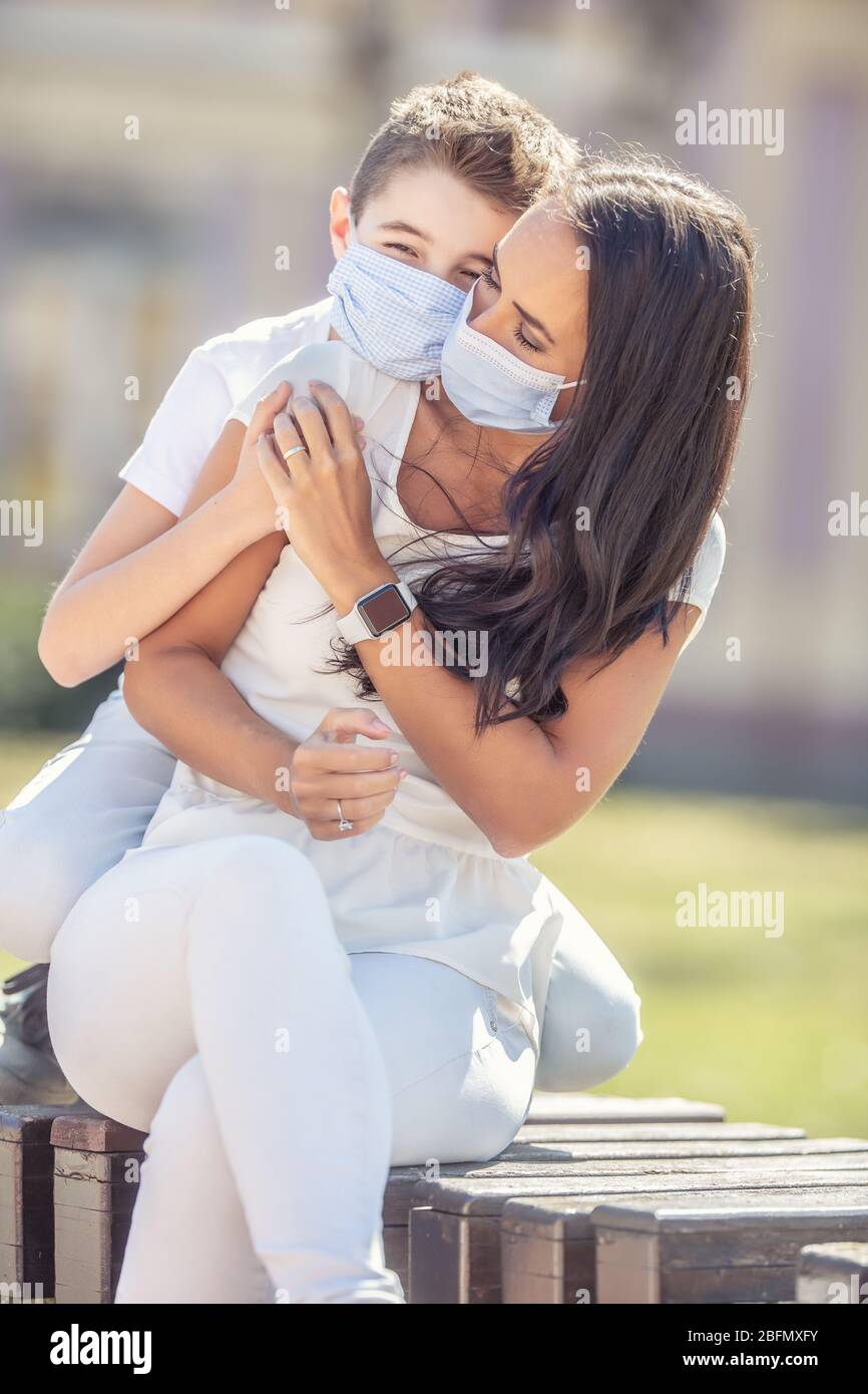 Ragazzo abbracciando la madre dalla schiena, tenendosi le mani all'aperto, con maschere facciali. Foto Stock
