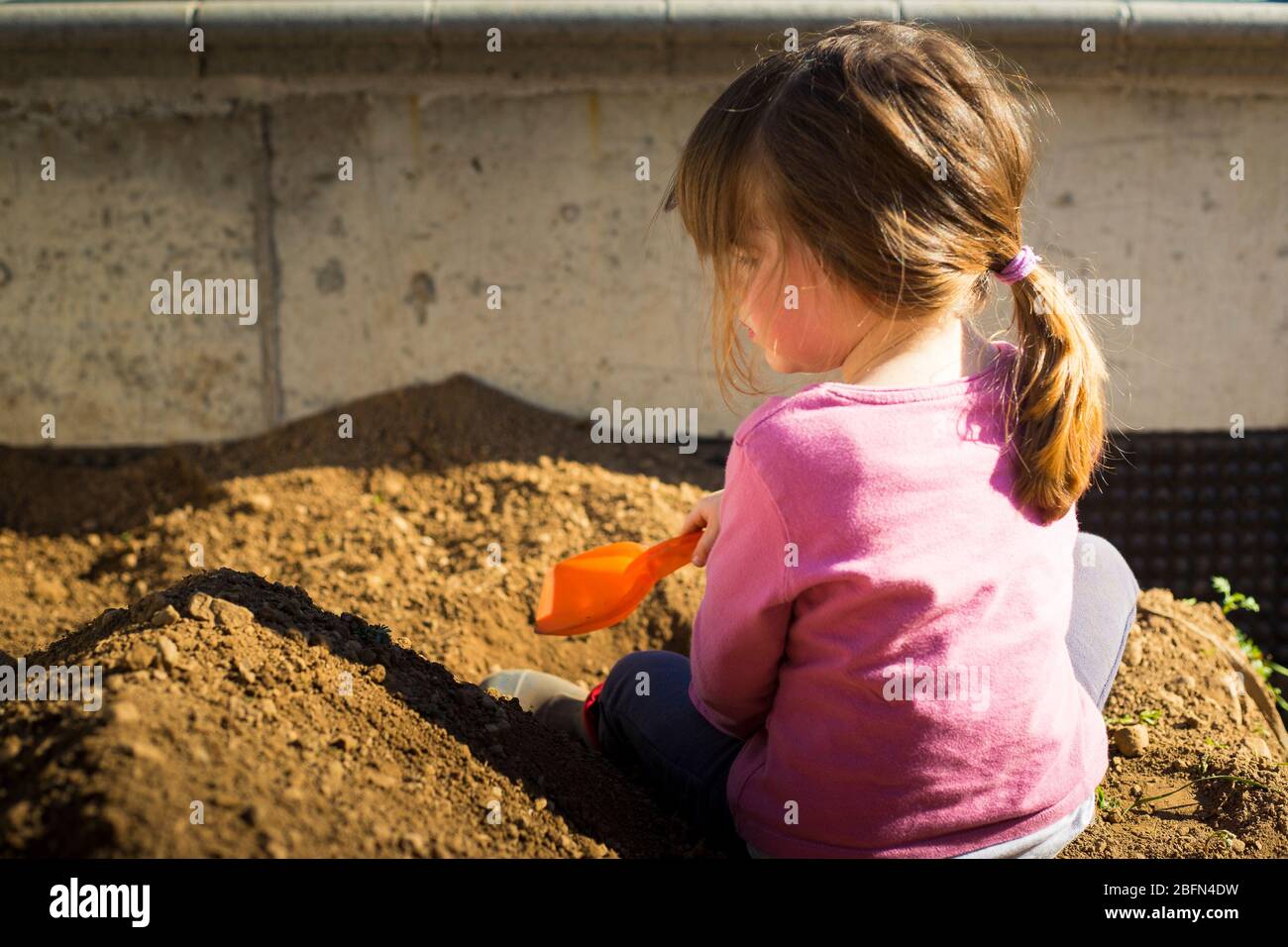 Bambina piccola scavando terreno con una paletta nel giardino durante il covid-19 pandemic lockdown. Attività all'aperto idea per i bambini durante il soggiorno a casa. Foto Stock