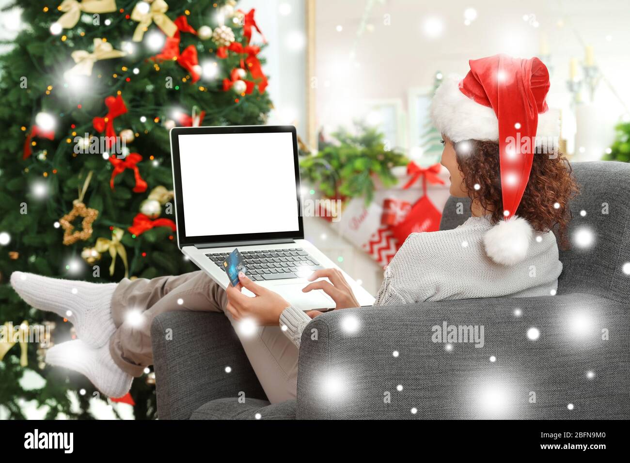 Donna shopping online con carta di credito a casa per Natale. Effetto neve. Natale concetto di shopping. Foto Stock