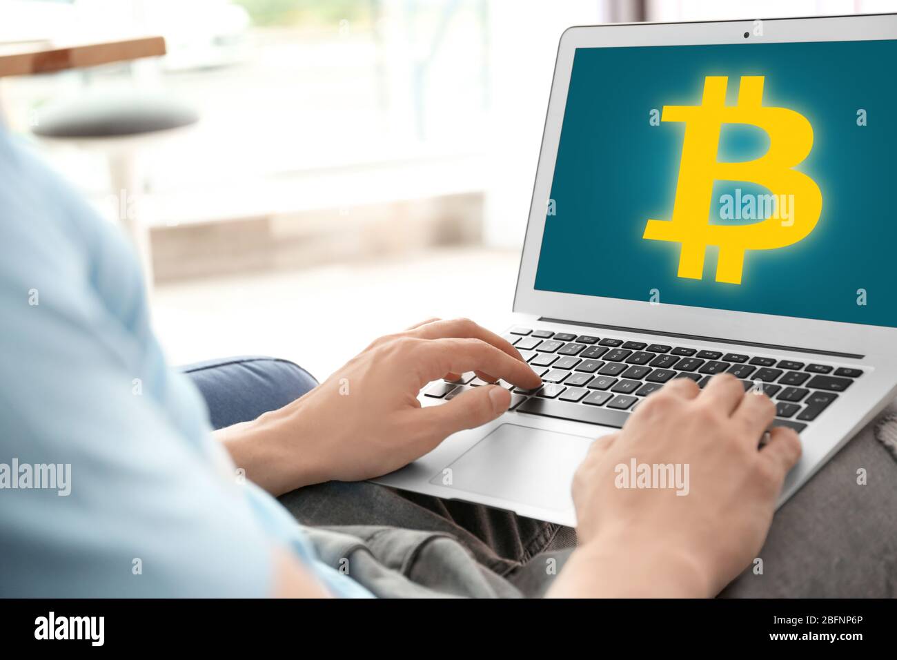 Uomo che usa un laptop con il simbolo della moneta a forma di bit sullo schermo a casa Foto Stock