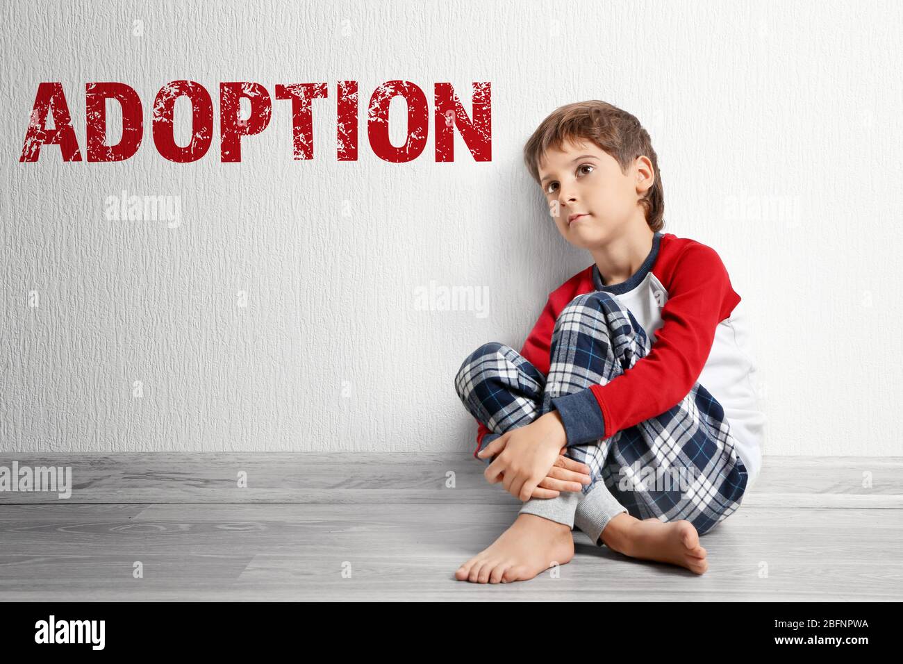 Concetto di adozione. Triste ragazzino seduto sul pavimento vicino al muro Foto Stock