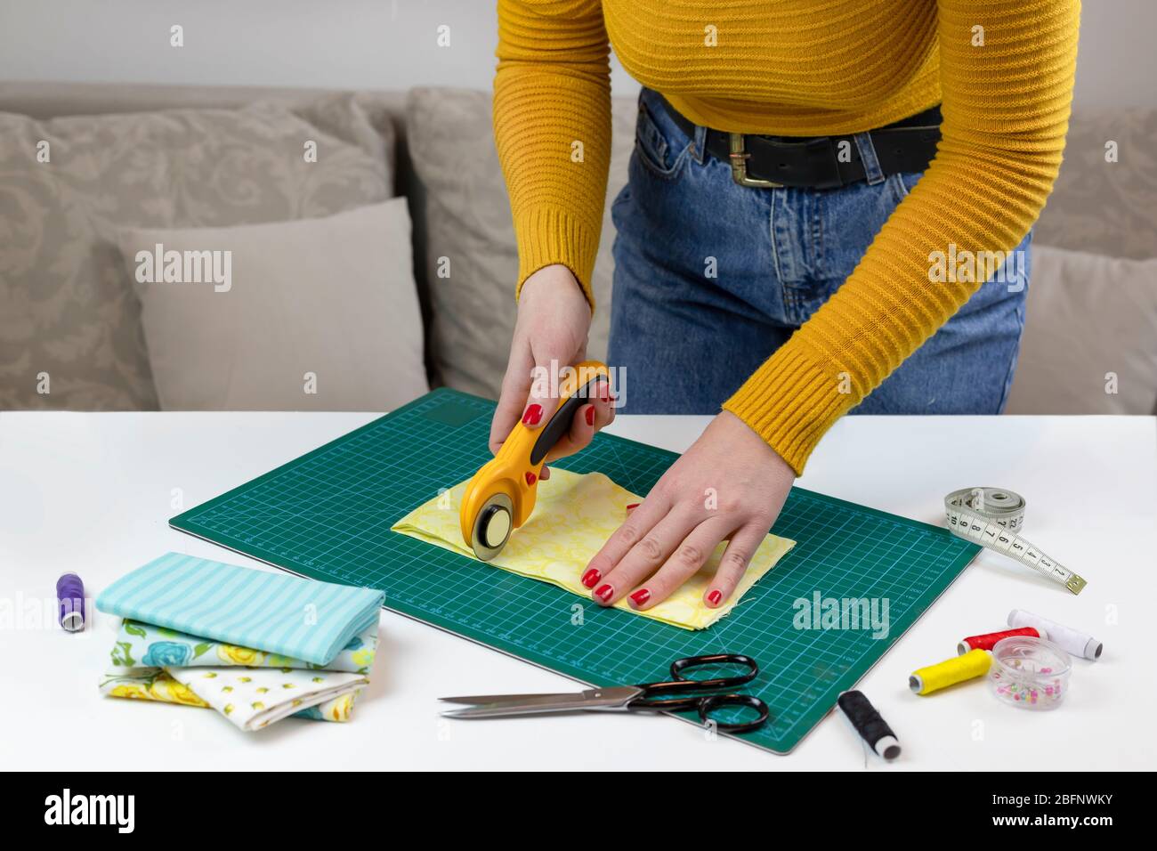 donna in un giallo taglia il tessuto. ci sono strumenti trapuntatura sul tavolo. coltello patchwork, forbici, foderato tappeto di taglio, auto-bloccaggio, filo, centimetro Foto Stock