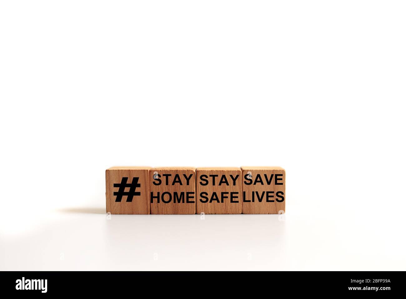 Immagine concettuale un blocco di legno e le parole RIMANGONO A CASA, RIMANGONO AL SICURO, SALVANO VITE CON una tazza di caffè bianco su sfondo bianco Foto Stock