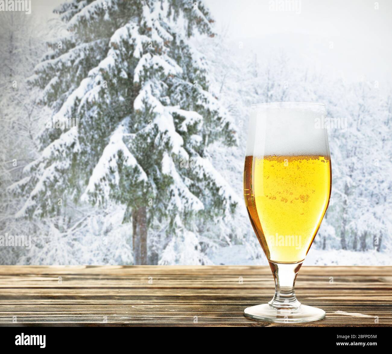 Bicchiere di birra su tavolo di legno contro sfondo invernale. Foto Stock