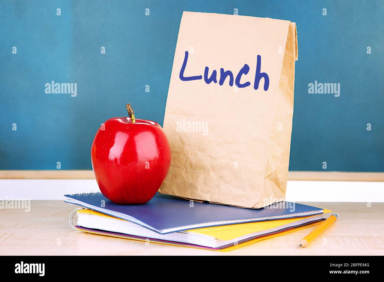 Concetto di pranzo a scuola. Sacchetto di carta, mela e cancelleria su tavolo di legno Foto Stock