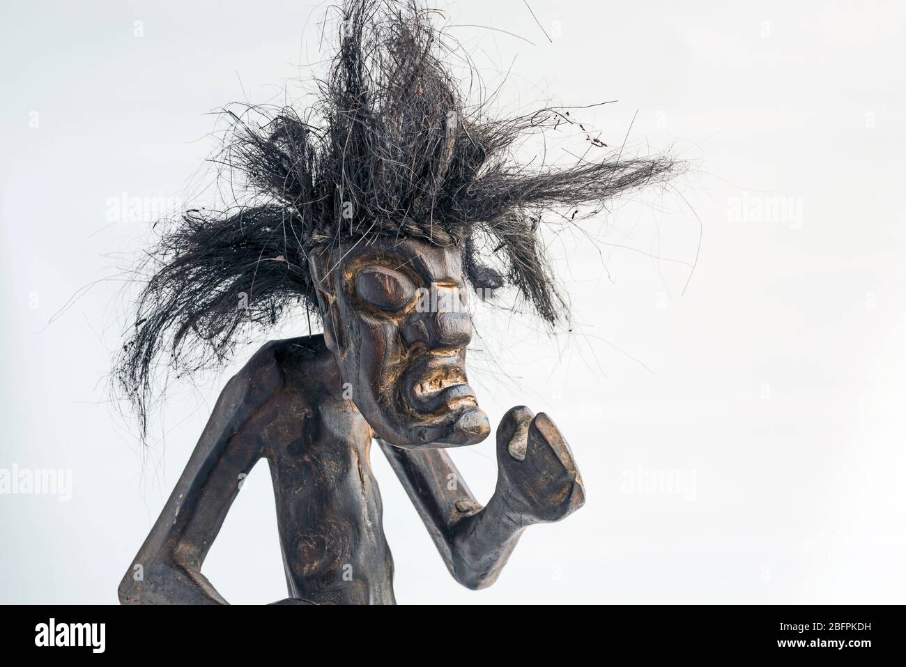 Figura intagliata in legno di uomo primitivo che indossa gonna di paglia e lunghi capelli neri a forma di tusled. Concetto; giorno difettoso dei capelli, differenza, nativo, selvaggio, unkempt, spaventoso. Foto Stock