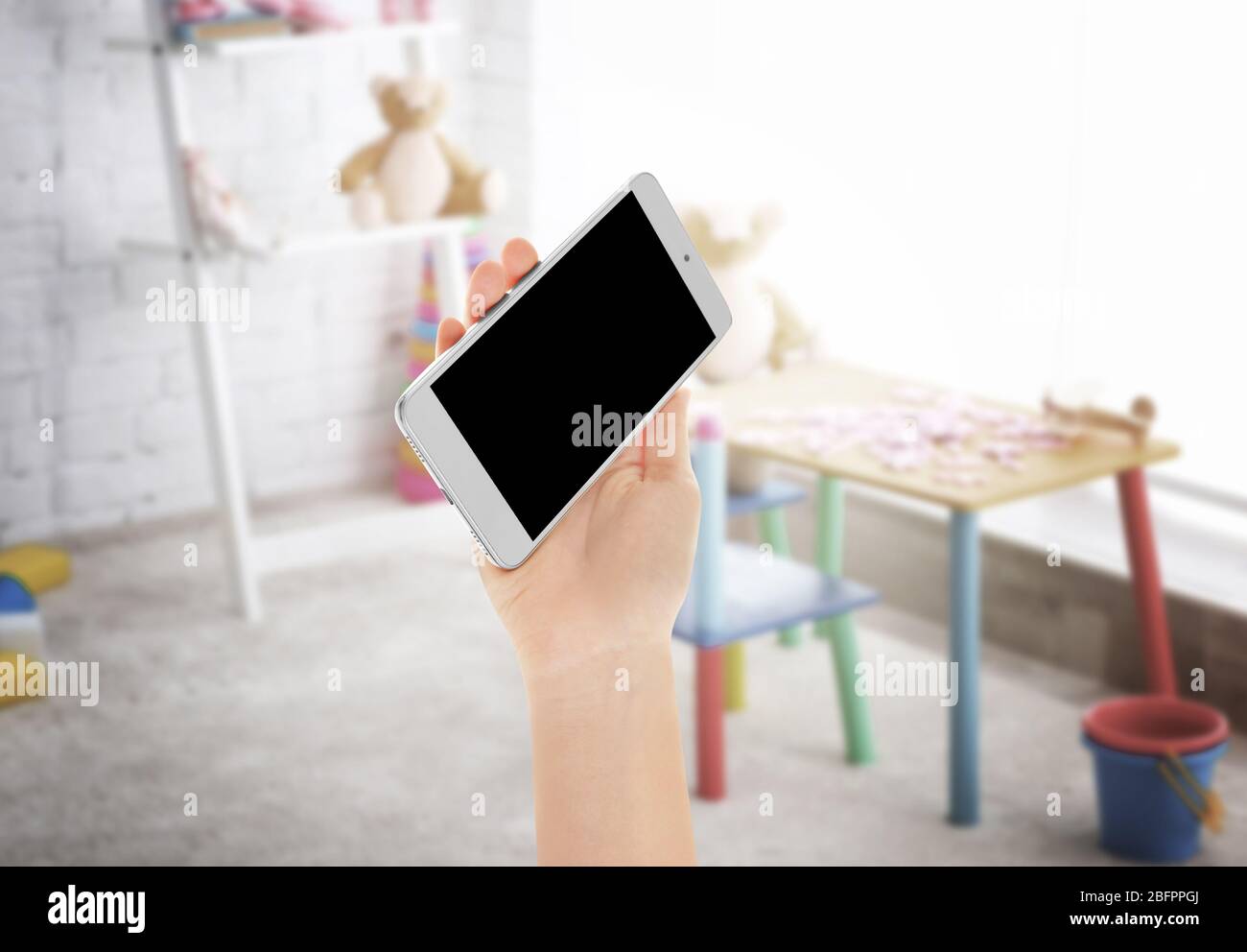 Insegnante che tiene uno smartphone con schermo vuoto e sala giochi sullo sfondo. Concetto di scuola e tecnologia moderna Foto Stock