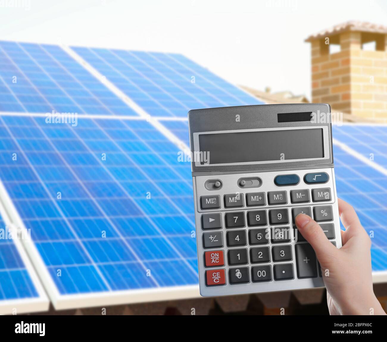 Donna che tiene calcolatrice e pannelli solari sullo sfondo. Riduzione delle spese per l'elettricità Foto Stock