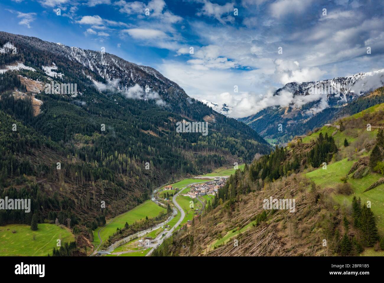 Veduta aerea della valle con verdi pendici delle montagne d'Italia, il Trentino, gli alberi caduti dal vento, enormi nuvole su una valle, verde Foto Stock